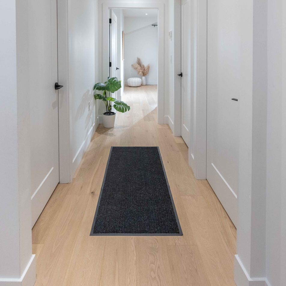 Long hallway with a black rug on light wood flooring