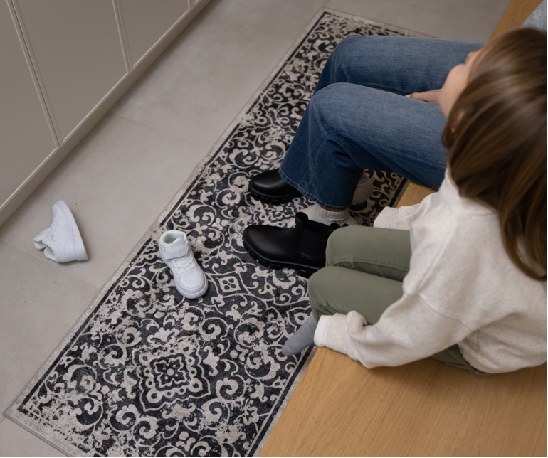 Person sitting on a patterned rug with shoes on the floor